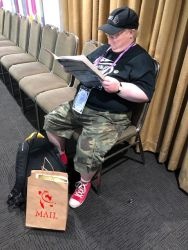 A convention attendee reading the Convention Book with their Convention Bag sitting by their feet.