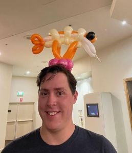 A man with a balloon creation on his head. It appears to be a prawn.