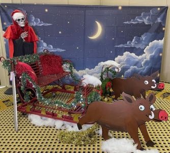 Death, dressed as the Hogfather, sits in the Hogfather's sleigh, pulled along by two paper piggies