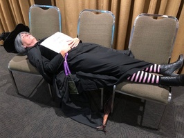 Granny Weatherwax lying down across a few chairs, holding a sign that reads "I ATEN'T DEAD"